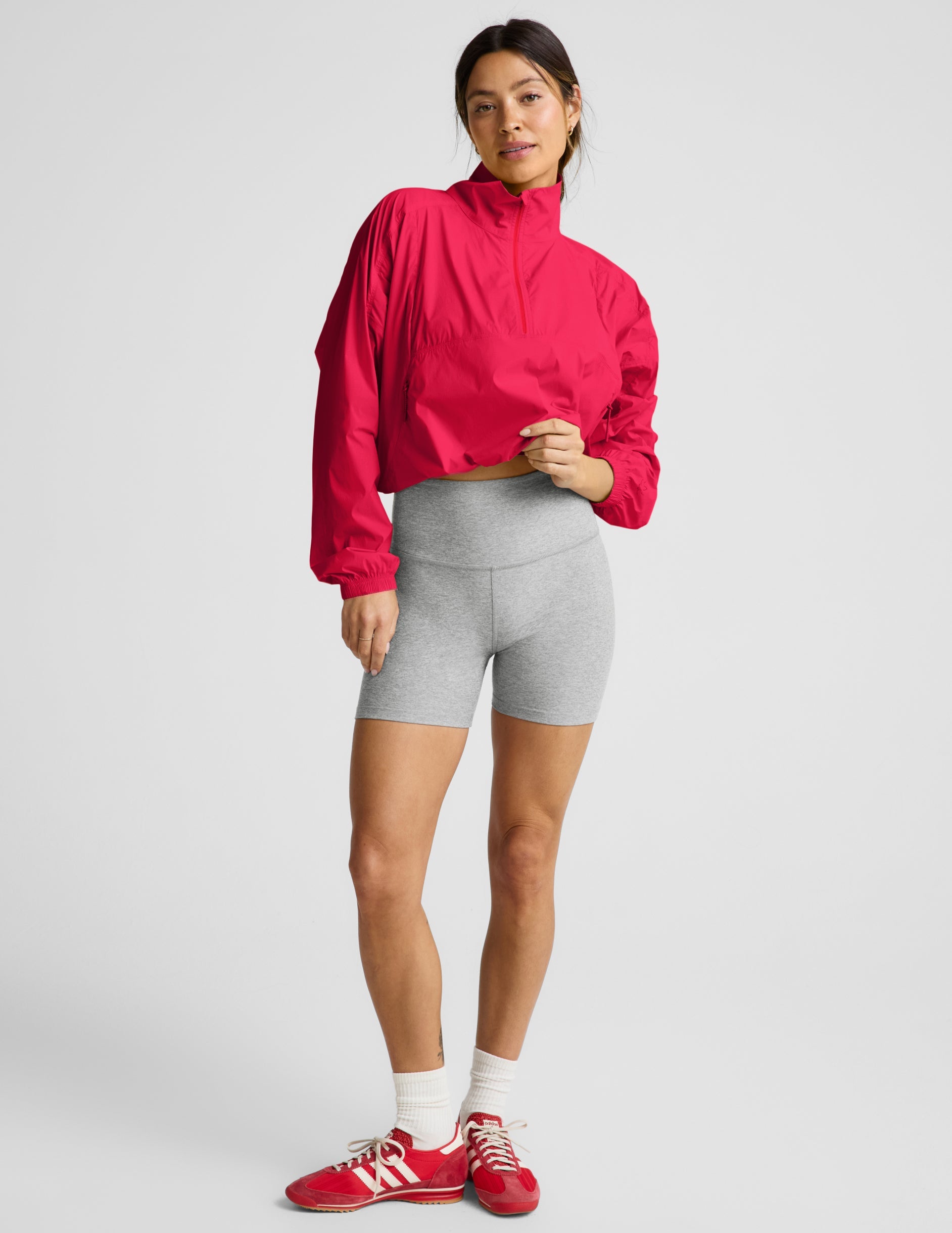 Woman wearing a bright red jacket and gray shorts on a light gray background.