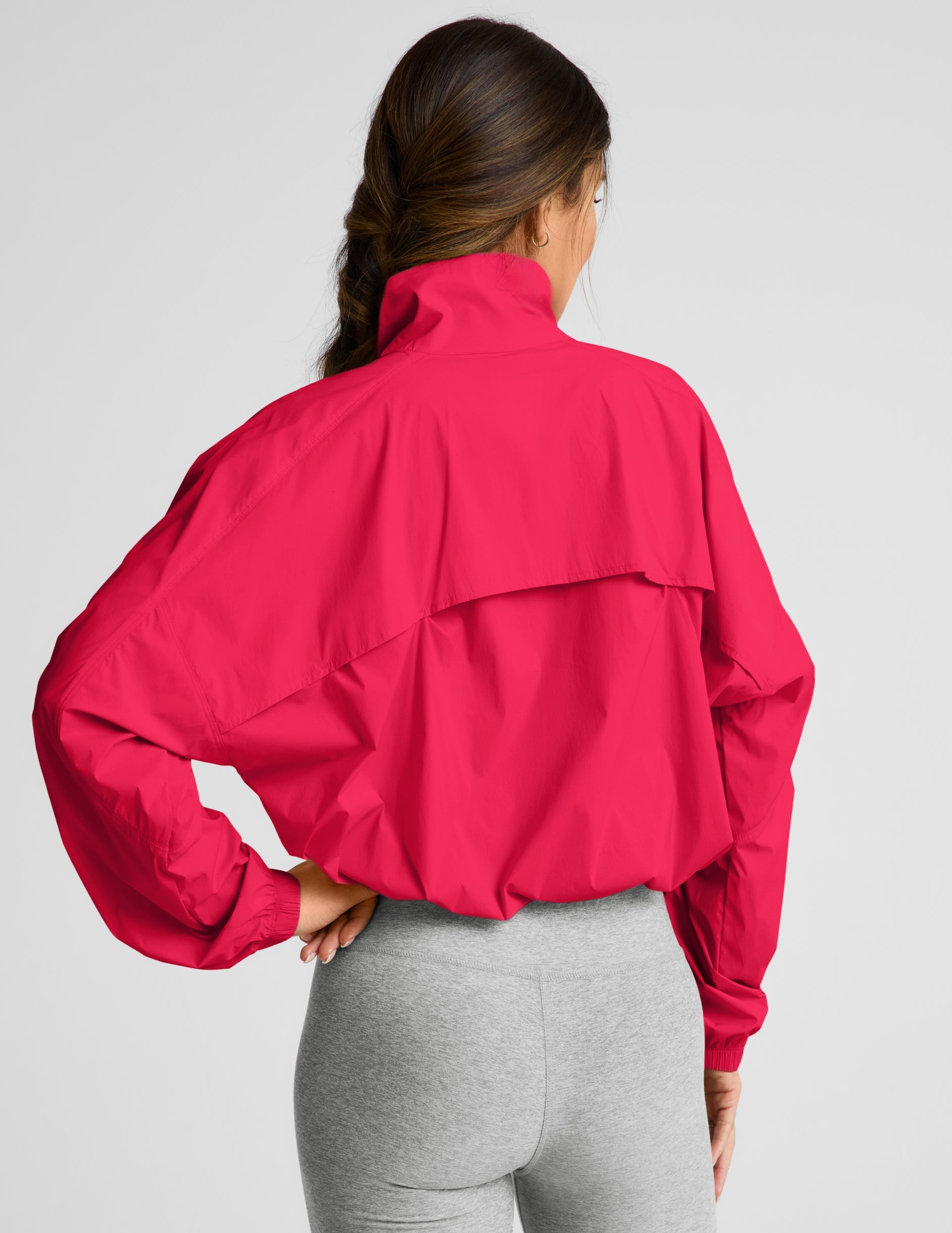 Woman wearing a bright red jacket and gray shorts on a light gray background.