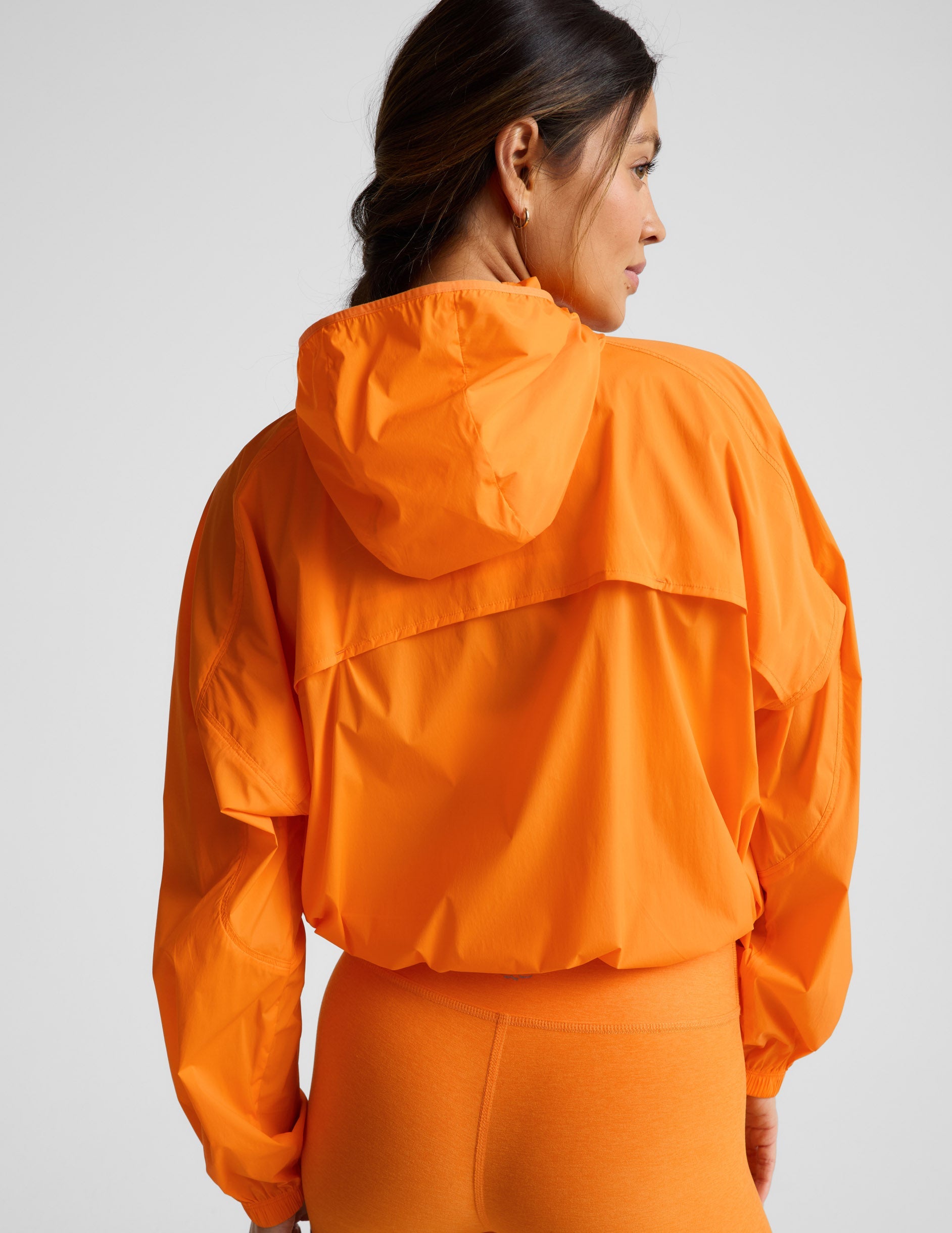 Woman wearing an orange jacket and orange biker shorts against a plain background.