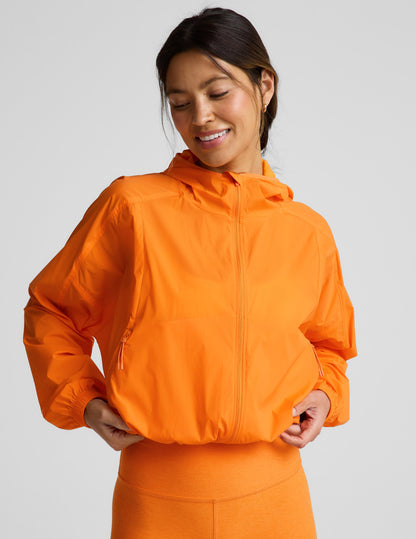 Woman wearing an orange jacket and orange biker shorts against a plain background.