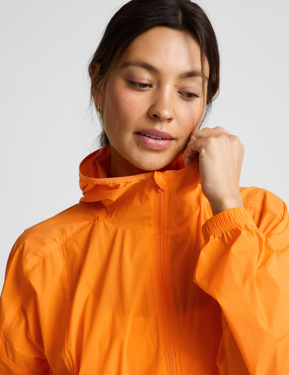 Woman wearing an orange jacket and orange biker shorts against a plain background.
