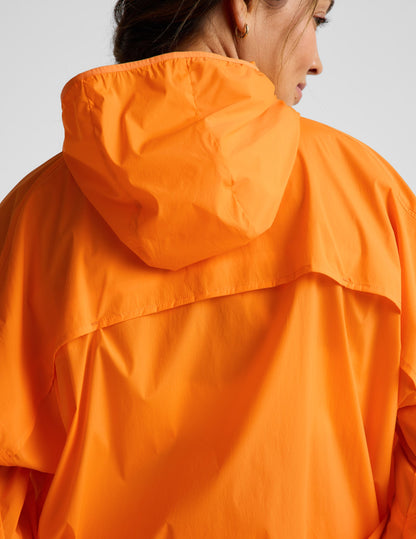 Woman wearing an orange jacket and orange biker shorts against a plain background.