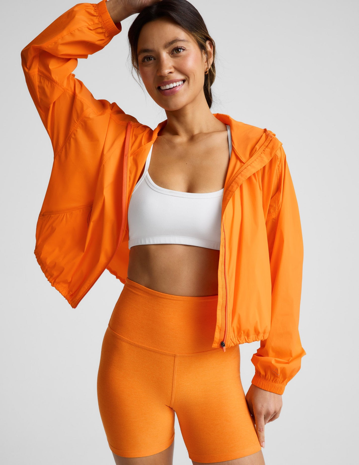 Woman wearing an orange jacket and orange biker shorts against a plain background.
