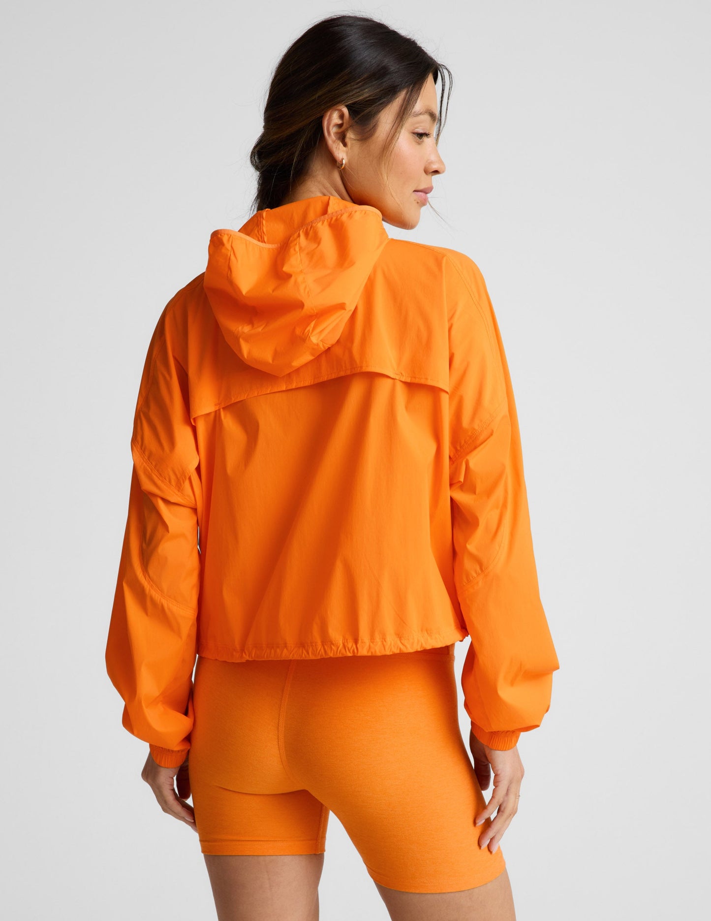 Woman wearing an orange jacket and orange biker shorts against a plain background.
