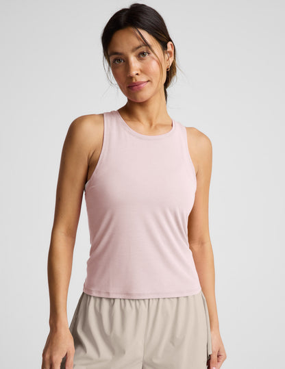 Woman wearing a pink sleeveless active tank and beige shorts against a plain background.