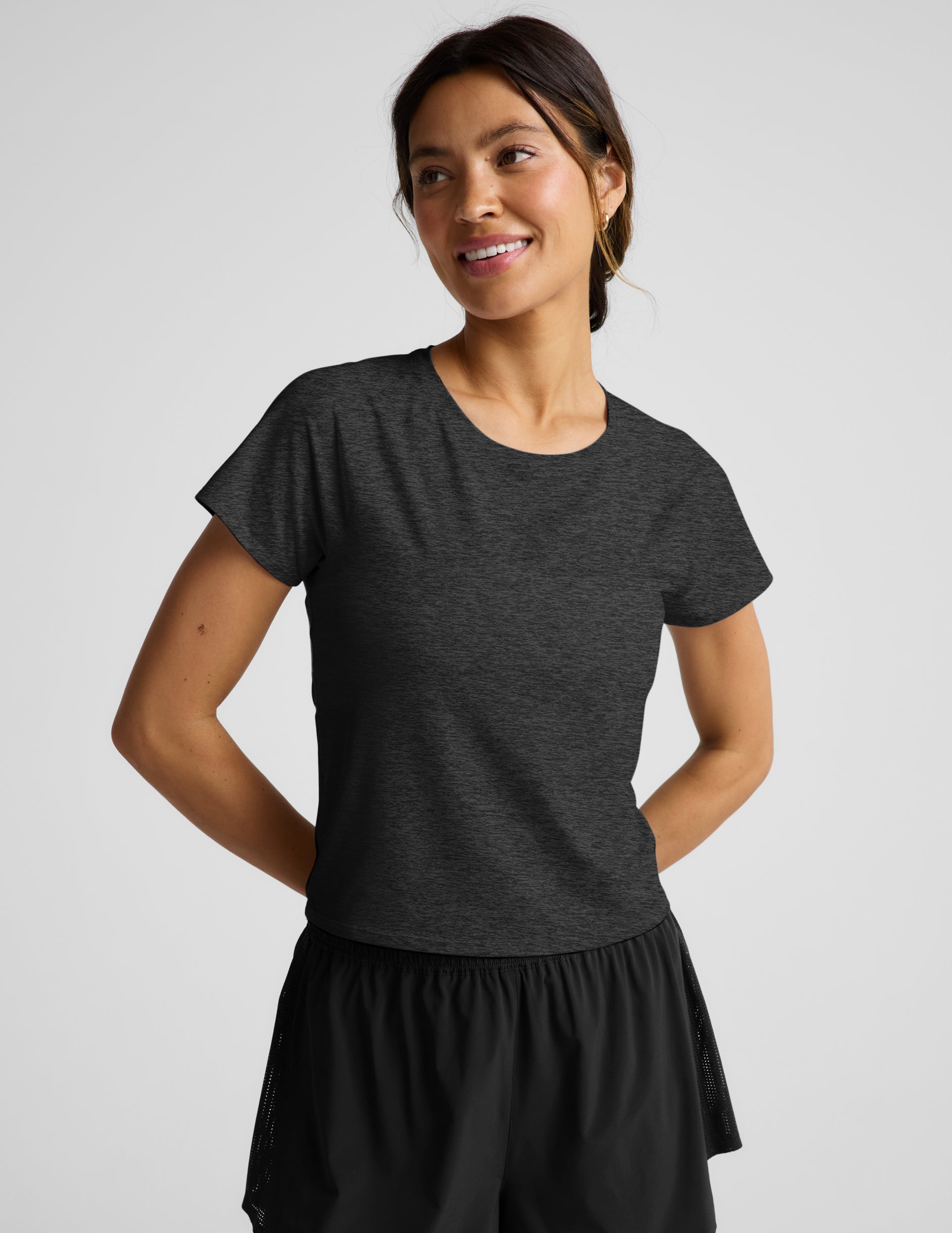 Woman wearing a dark gray t-shirt and black shorts on a light gray background.