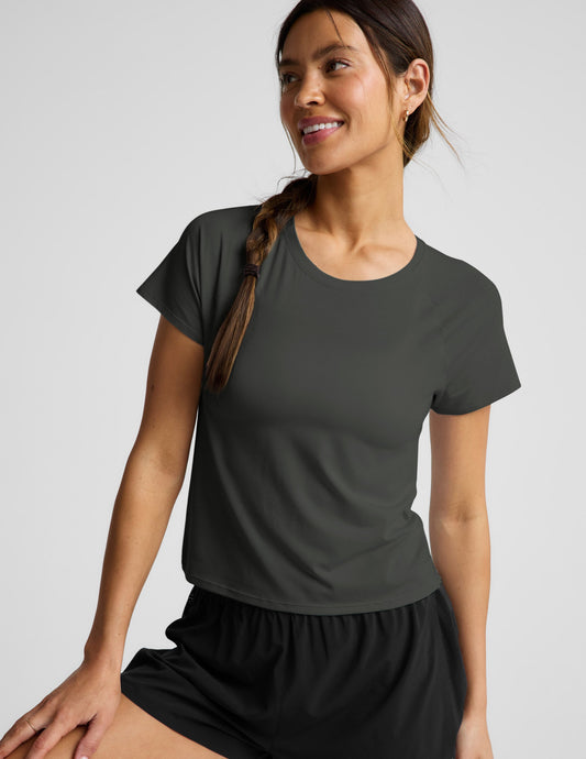 Woman wearing a dark green short sleeve active top and black shorts against a plain background.
