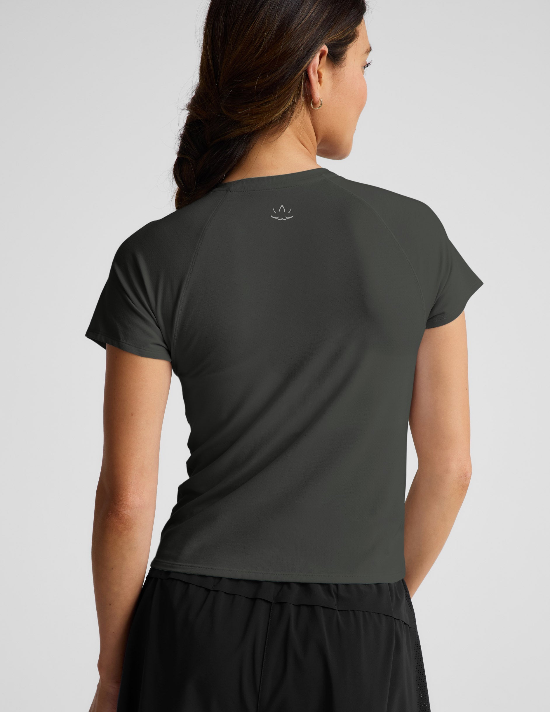Woman wearing a dark green short sleeve active top and black shorts against a plain background.