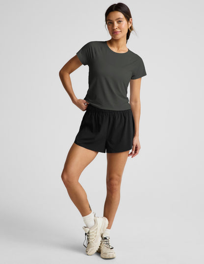 Woman wearing a dark green short sleeve active top and black shorts against a plain background.