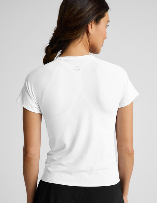 Woman wearing a white short sleeve active top and black shorts against a plain background.