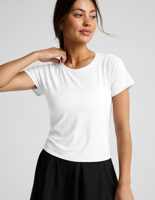 Woman wearing a white short sleeve active top and black shorts against a plain background.