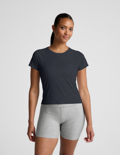 Woman wearing a navy blue active short sleeve top and gray biker shorts against a plain background.