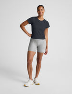 Woman wearing a navy blue active short sleeve top and gray biker shorts against a plain background.
