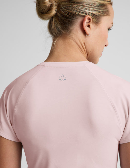 Woman wearing a light pink active short sleeve top and pink running shorts against a plain background.