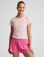 Woman wearing a light pink active short sleeve top and pink running shorts against a plain background.