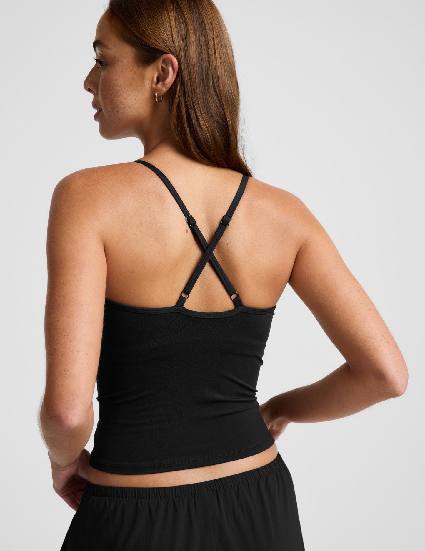 Woman wearing a black cowl neck tank top and black pants against a plain background.