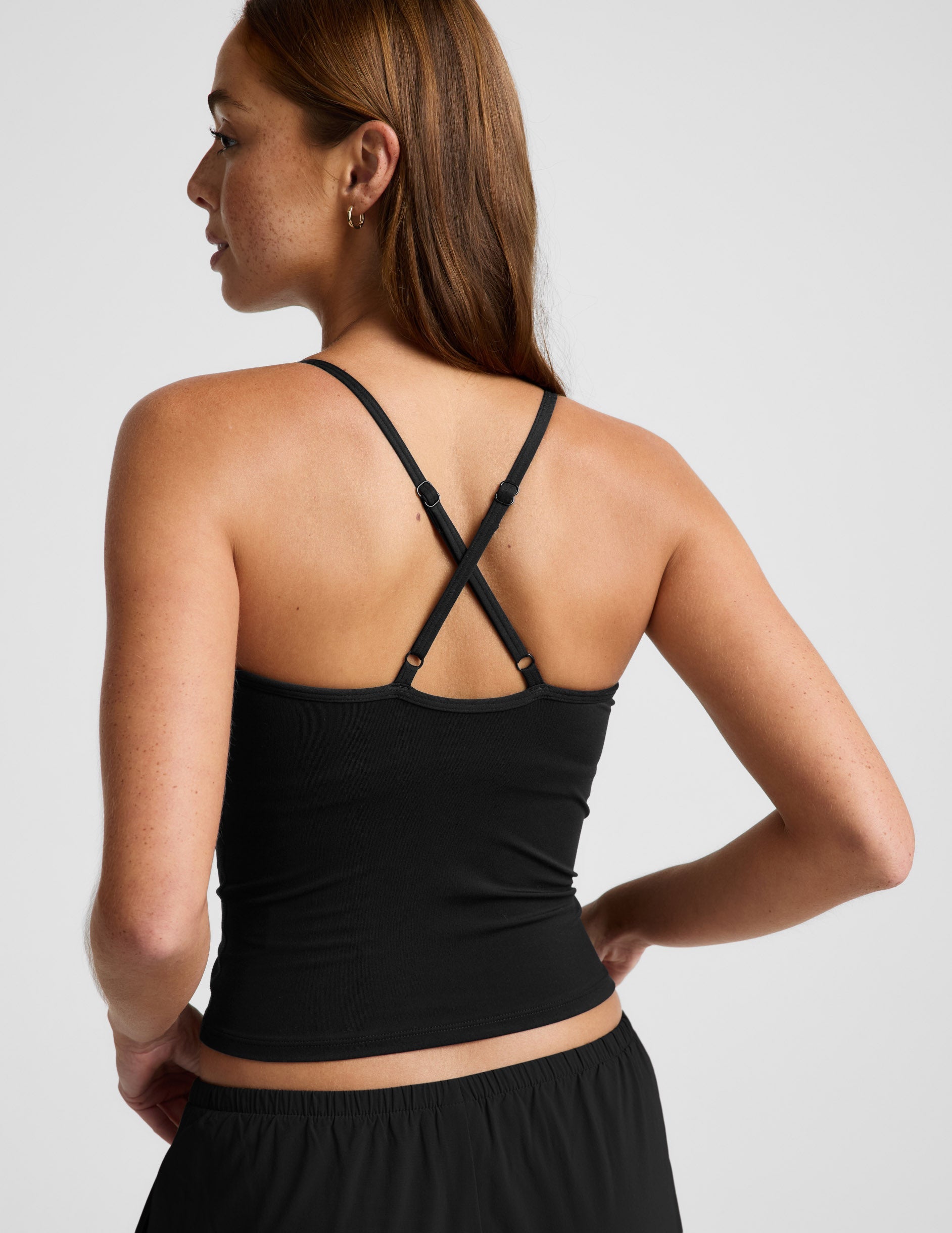 Woman wearing a black cowl neck tank top and black pants against a plain background.