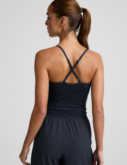 Woman wearing a navy cowl neck tank top and blue trousers against a plain background.