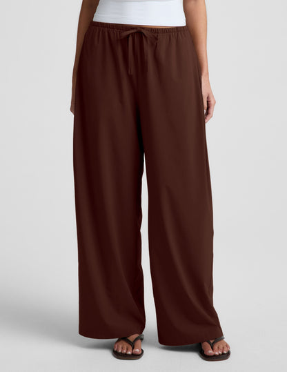 Woman wearing Brown Solstice Drawstring Wide Leg Pant 29" with a tie-waist, paired with a white top and dark flip-flops.