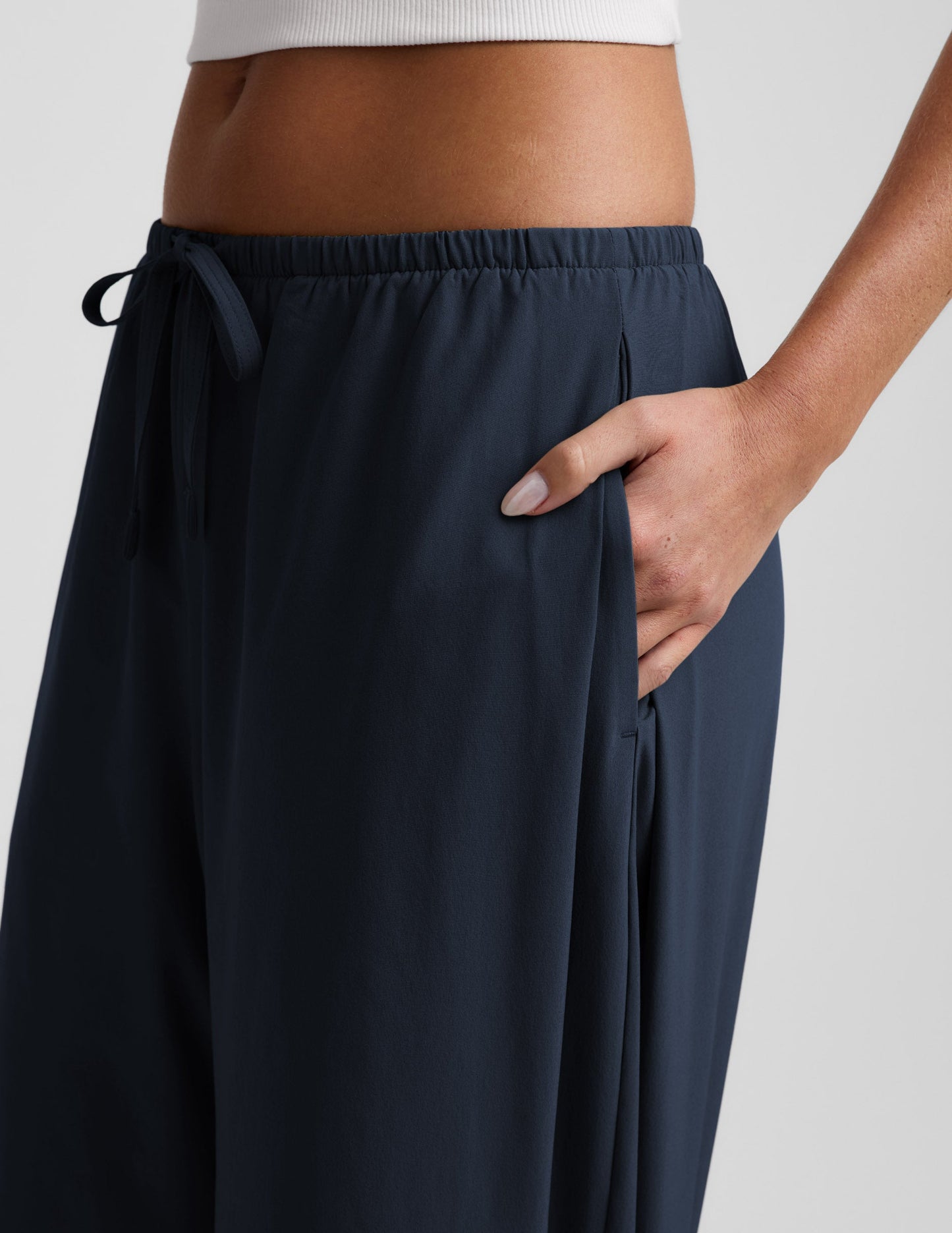 Woman wearing navy Solstice™ Drawstring Wide Leg Pant 29" with hand in side seam pocket and white ribbed top, side profile.