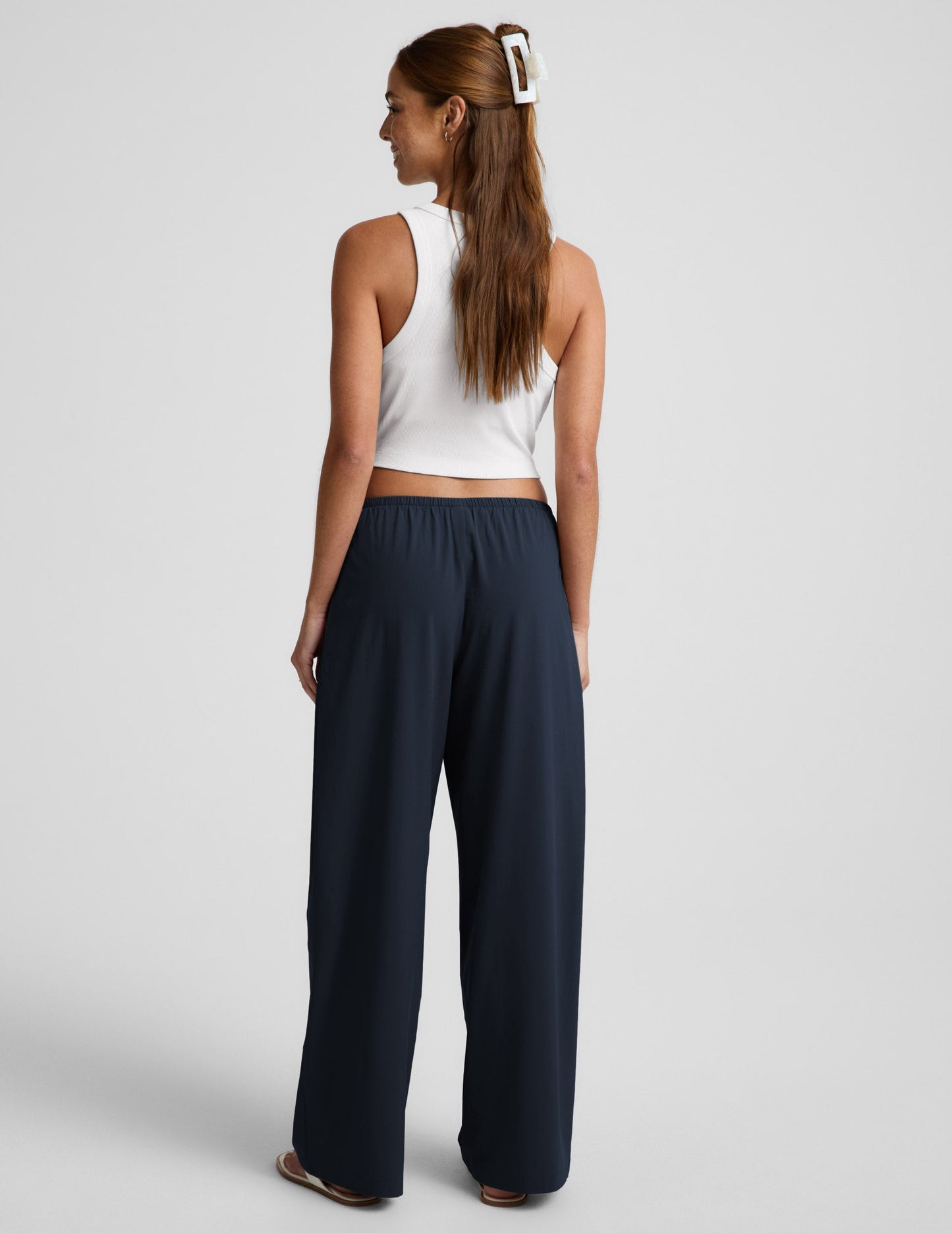 Woman wearing navy Solstice Drawstring Wide Leg Pant 29" paired with a white cropped tank top, rear view.