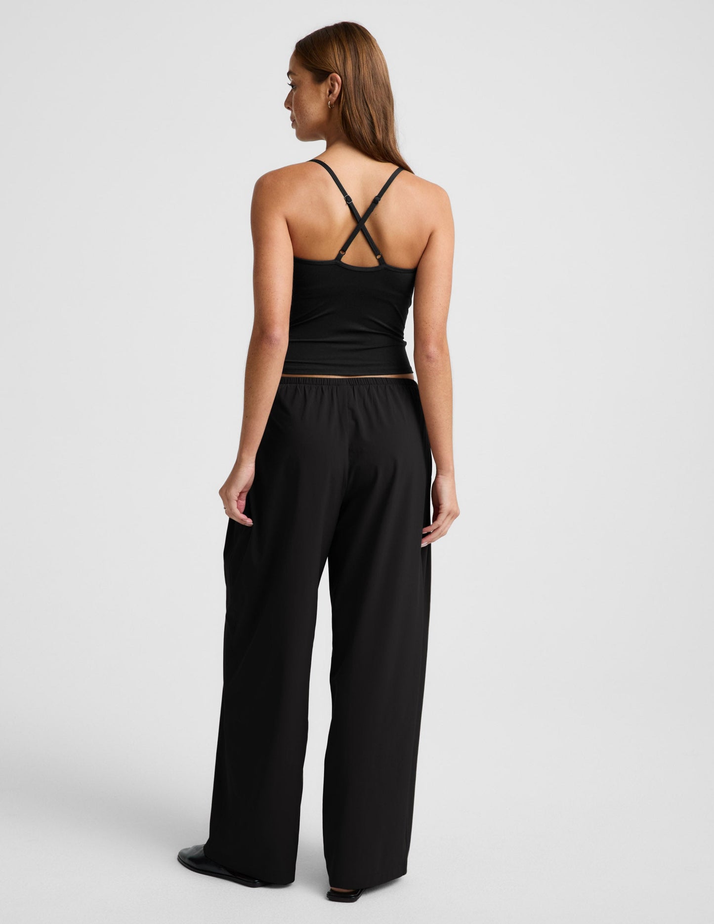 Woman wearing black Solstice Drawstring Wide Leg Pant 31™ from a rear view, paired with a black strappy tank top.