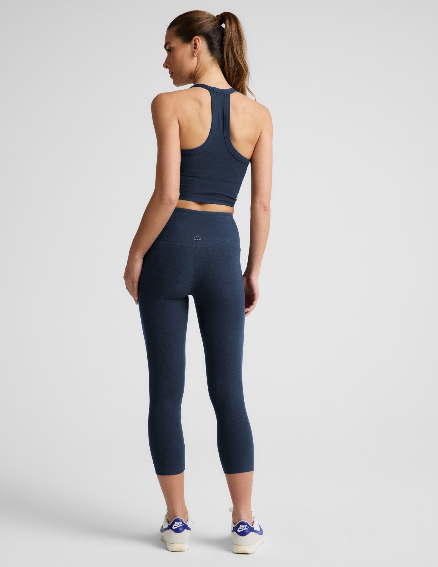 Rear view of woman wearing Navy Spacedye Walk And Talk High Waisted Capri Legging paired with a matching tank and sneakers.