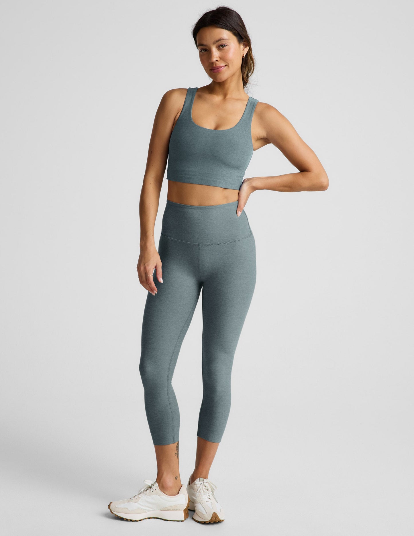 Woman wearing Green Spacedye Walk And Talk High Waisted Capri Legging with a matching sports bra and cream sneakers.