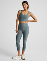 Woman wearing Green Spacedye Walk And Talk High Waisted Capri Legging with a matching sports bra and cream sneakers.