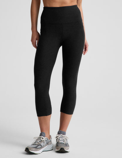 Woman wearing Black Spacedye™ Out Of Pocket High Waisted 20.5" Capri Legging with side pockets and grey sneakers.