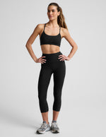 Woman wearing Black Spacedye™ Out Of Pocket High Waisted 20.5" Capri Legging with a matching sports bra and sneakers.