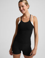 Woman wearing a black and white layered tank and shorts against a plain background.