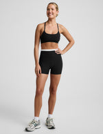 Woman wearing Black Spacedye™ Layered 3" Short with a white contrast waistband, paired with a black sports bra and sneakers.