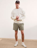 Front view of olive Saturday Men's Short on a model, paired with a cream sweatshirt, baseball cap, and white sneakers.