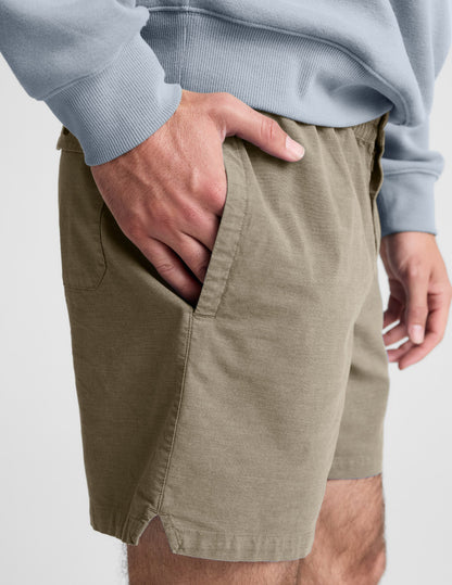 Close-up of olive Saturday Men's Short showing hand in pocket, elastic waistband, and soft peached fabric.