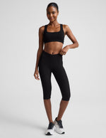 Woman wearing Black Impulse™ Ribbed V-Waist Pedal Pusher Legging paired with a black sports bra and white sneakers.