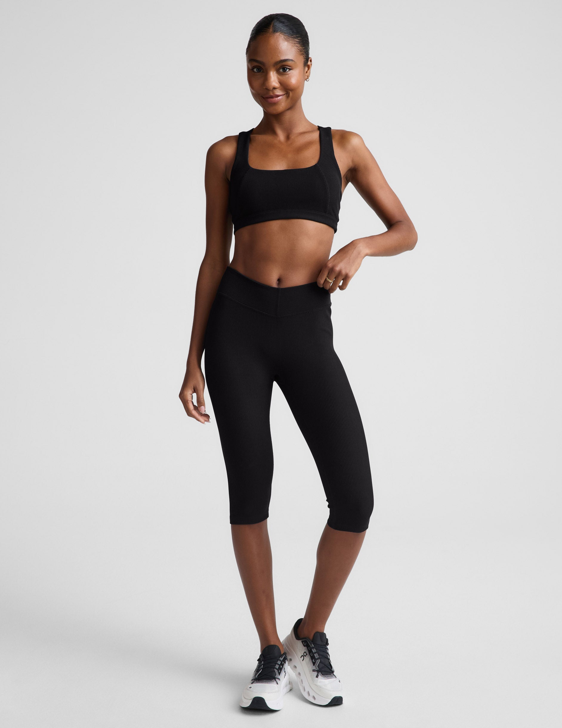 Woman wearing Black Impulse™ Ribbed V-Waist Pedal Pusher Legging paired with a black sports bra and white sneakers.
