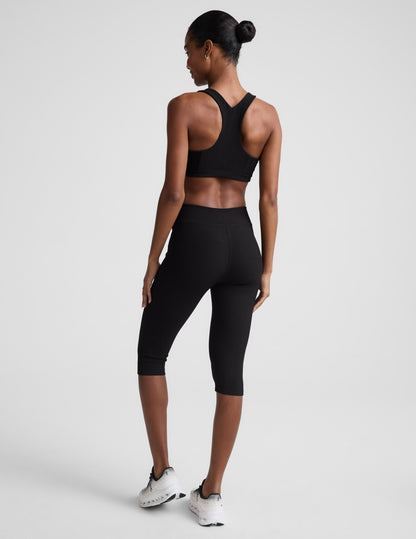 Rear view of woman wearing Black Impulse™ Ribbed V-Waist Pedal Pusher Legging paired with a black sports bra and sneakers.