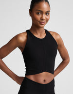Woman wearing a black cropped ribbed tank and shorts against a plain background.
