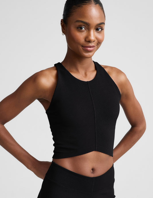Woman wearing a black cropped ribbed tank and shorts against a plain background.