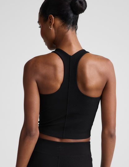 Woman wearing a black cropped ribbed tank and shorts against a plain background.