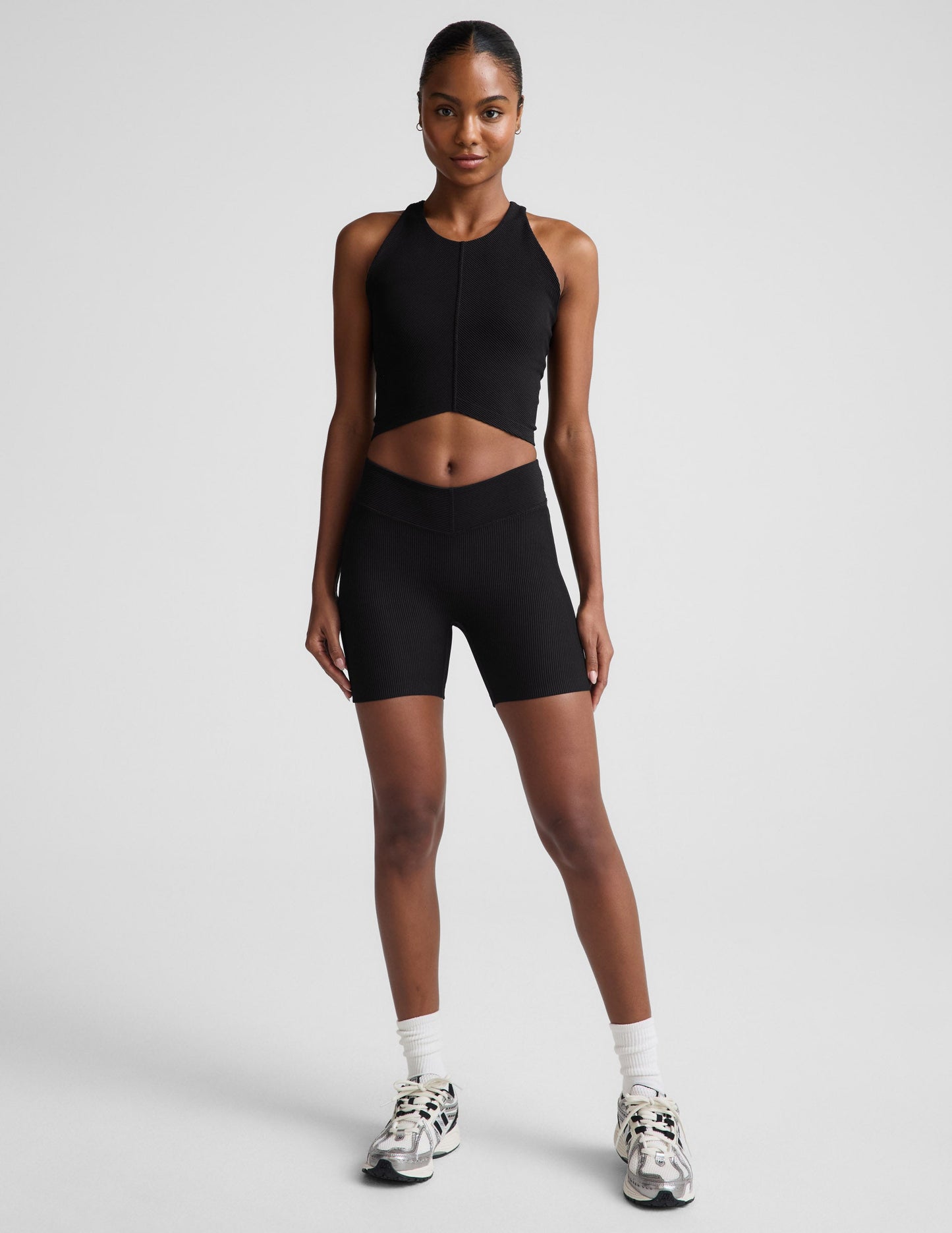 Woman wearing Black Impulse™ Ribbed V-Waist 5" Biker Short paired with a matching black cropped tank top and white crew socks.