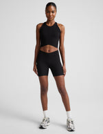 Woman wearing Black Impulse™ Ribbed V-Waist 5" Biker Short paired with a matching black cropped tank top and white crew socks.