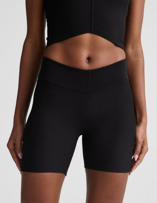Woman wearing Black Impulse Ribbed V-Waist 5" Biker Short paired with a matching ribbed crop top. Front view.