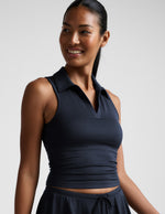 Woman wearing a blue sleeveless top with a collar against a plain background.