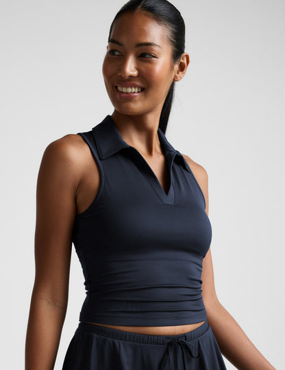 Woman wearing a blue sleeveless top with a collar against a plain background.