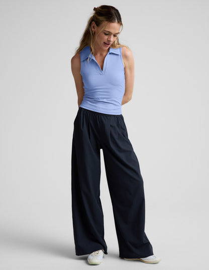 Woman wearing a light blue sleeveless polo shirt and black pants on a plain background.