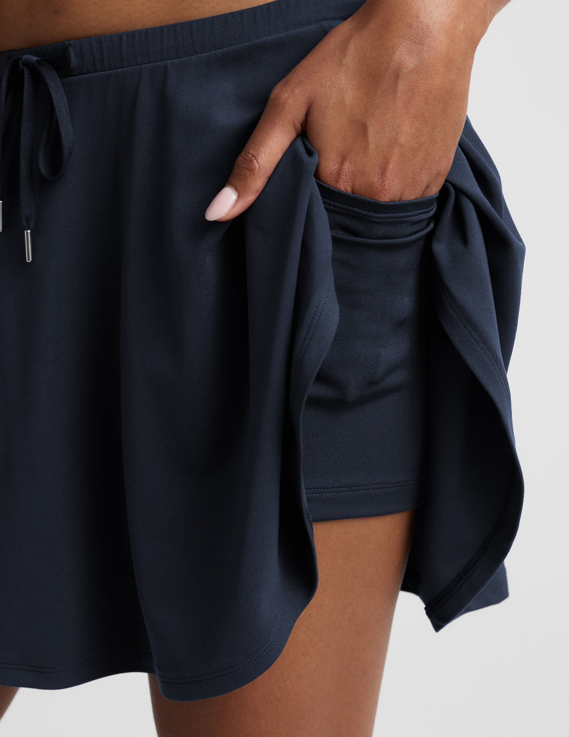 Close-up of Navy Sport Active Drawcord Mini Skirt showing a hand using the pocket in the built-in shorts.