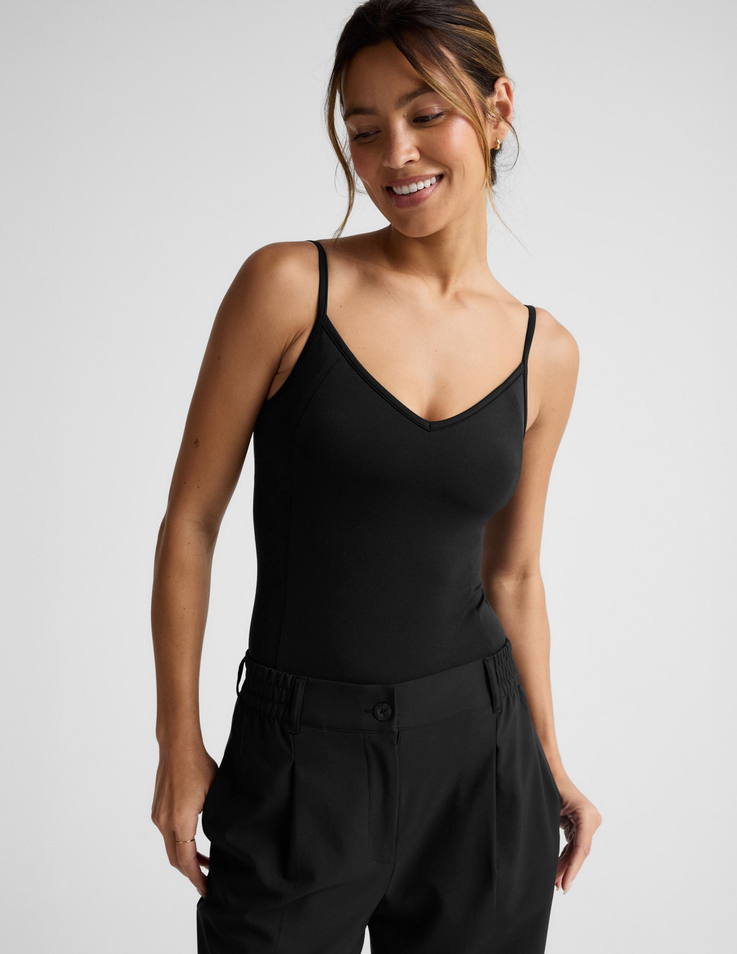 Woman wearing a black bodysuit and black pants against a plain background.