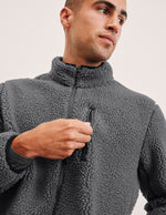 man wearing a gray fleece zip-up jacket against a plain background.